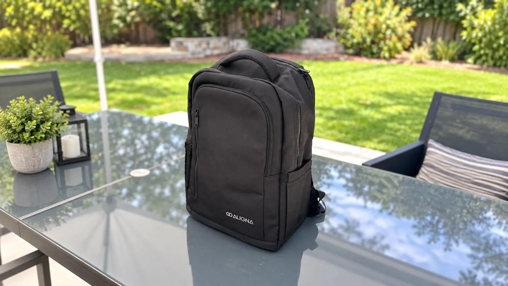The Align Pack, a black laptop backpack, standing on a glass table in a sunlit garden